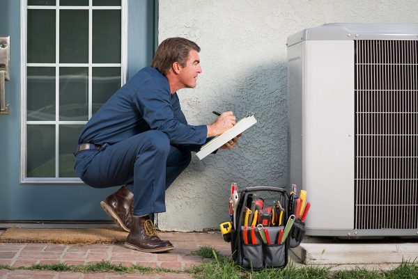 man holding clipboard inspecting a condensing unit outside